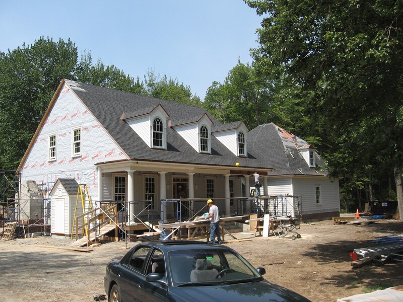 Gray asphalt roofing installation on new construction of white house with porch columns