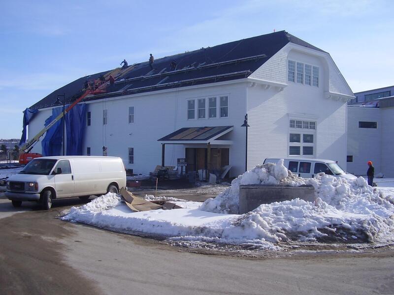 Black asphalt shingle roofing installation in winter on white barn